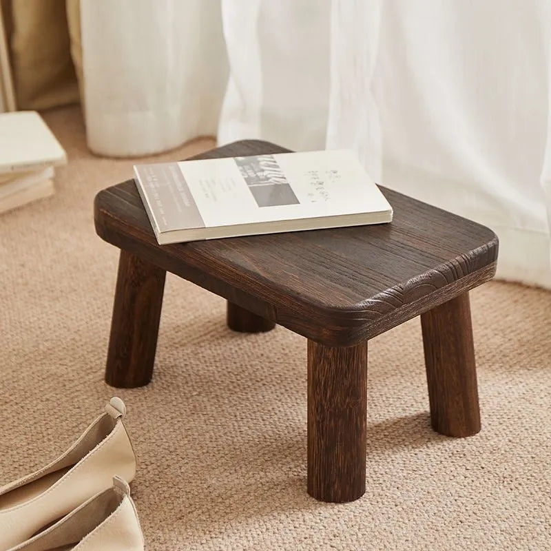Solid wood distressed finish changing stool with bracket structure legs in a living room setting.