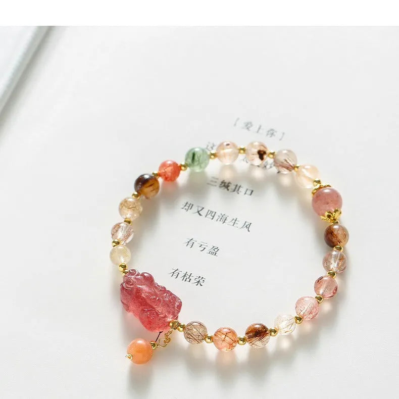 Copper women's bracelet with strawberry quartz crystal, Pixiu charm, and pearl accents on a white background.