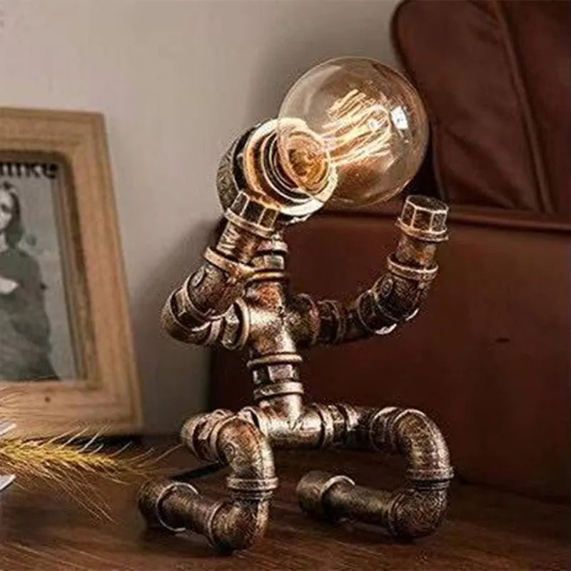 Custom industrial retro style iron pipe robot table lamp on a wooden desk.