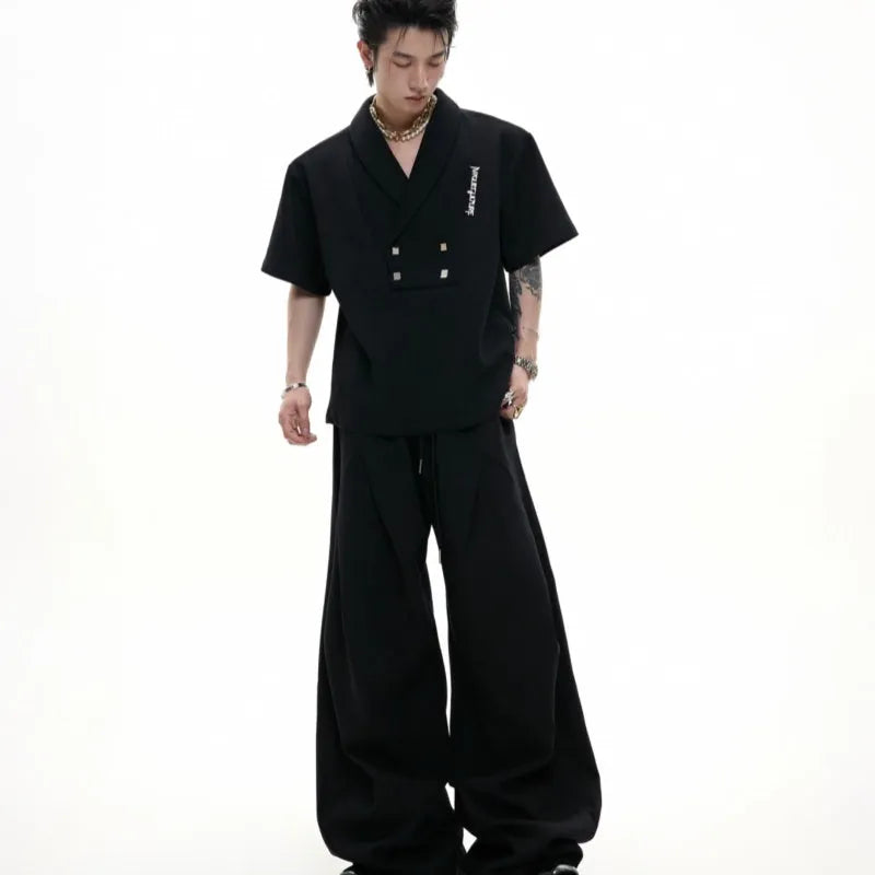 Men's dark grey cotton sports suit with V-neck top featuring padded shoulders and metal embellishments, paired with matching shorts.
