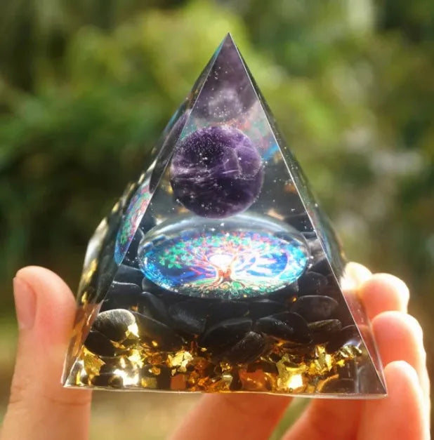 Clear epoxy resin pyramid ornament with natural crystal gravel inside on a wooden surface.