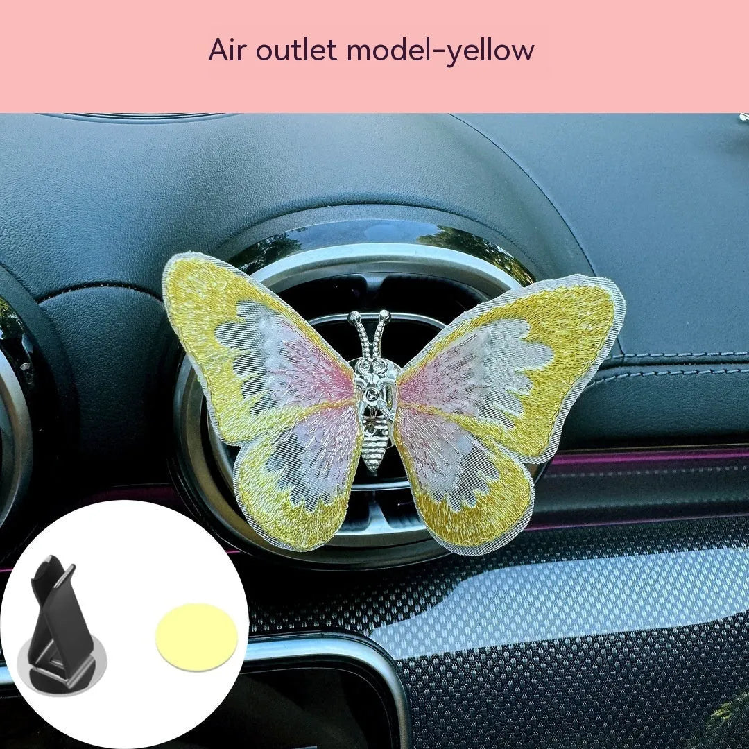 Fabric embroidered butterfly car air vent decoration in multiple colour options on a dashboard.