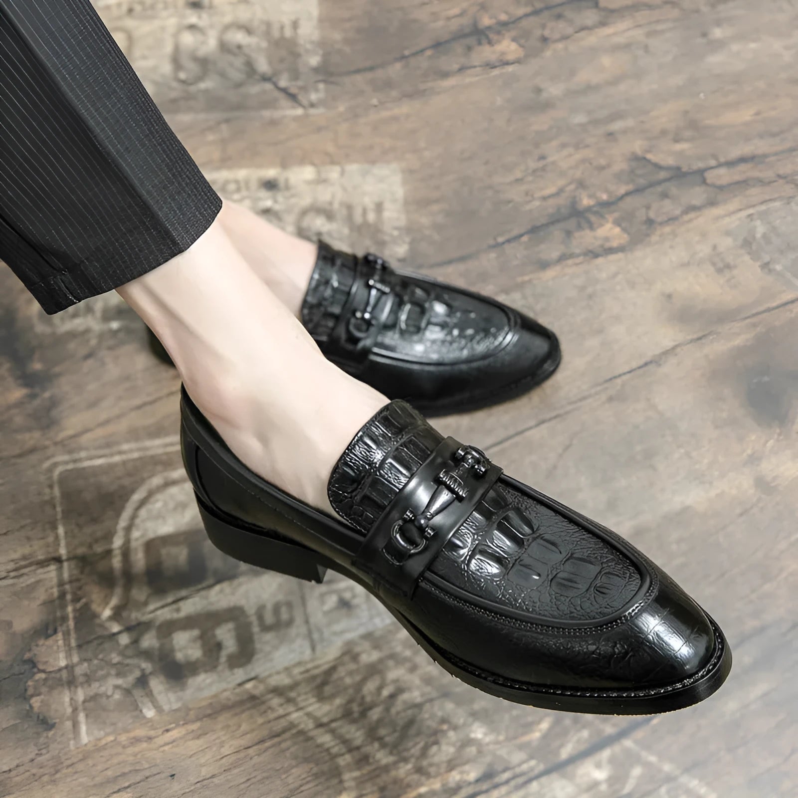 Men's black slip-on formal shoes with pointed toe and belt buckle detail on a light background