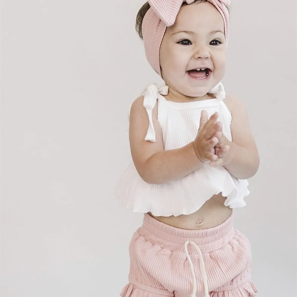 Baby girls white knitted cotton vest and pink shorts set on a light background