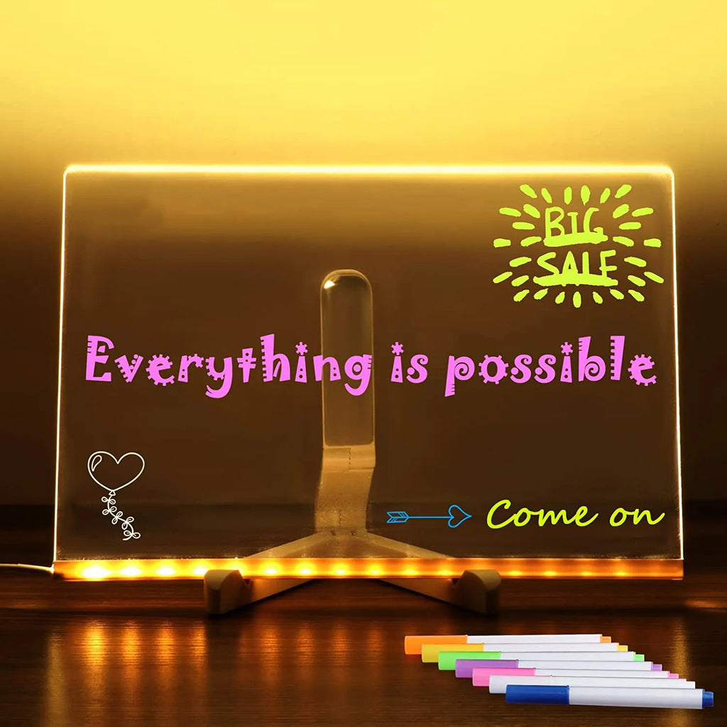 DIY acrylic LED message board lamp on a desk with colourful writing, showing USB cable and pens.