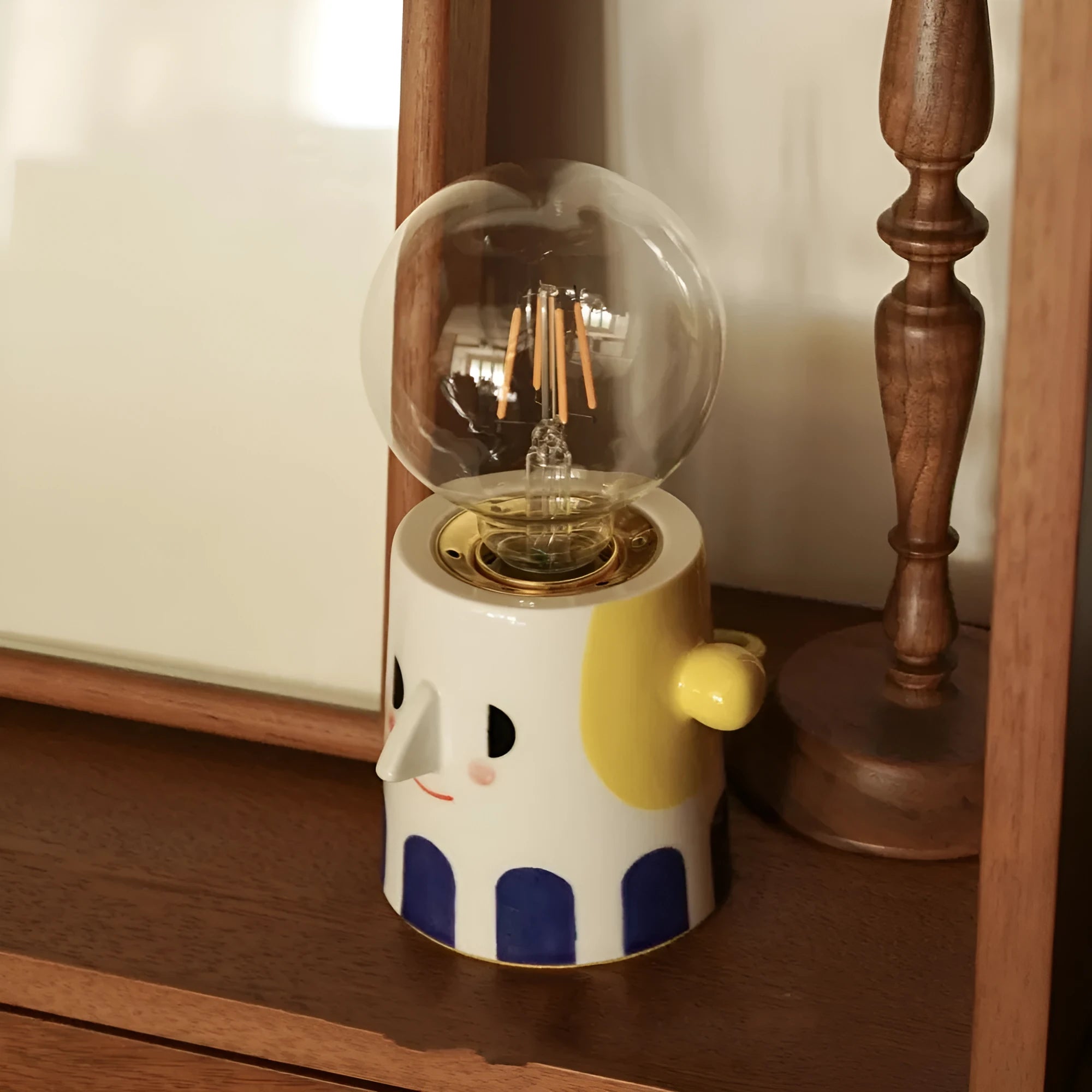 Handmade ceramic table lamp with a white ball headlight shade on a wooden table.