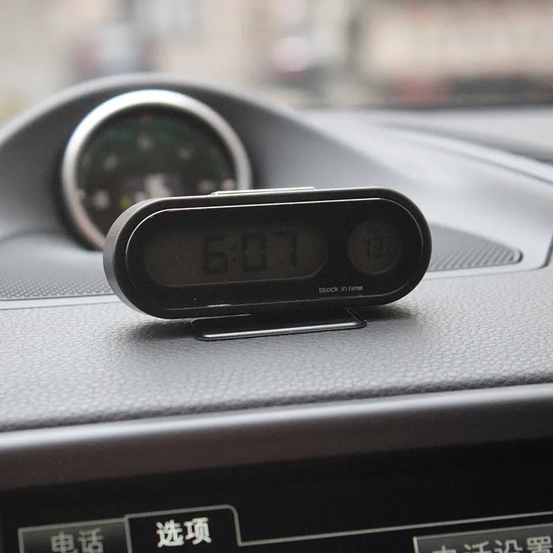 Black electronic car clock and thermometer with luminous digital display on an adjustable dashboard mount.