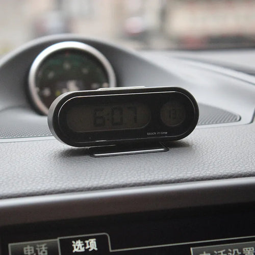 Black electronic car clock and thermometer with luminous digital display on an adjustable dashboard mount.