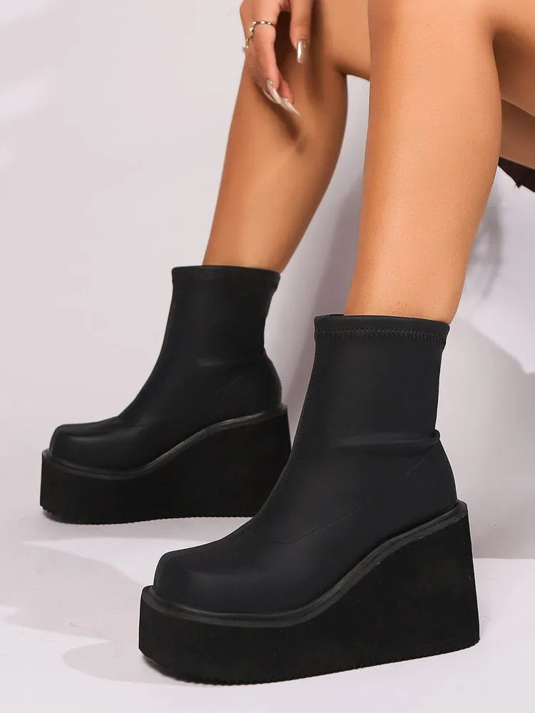Plus size black wedge heel ankle boots with a round toe and waterproof platform on a wooden floor.