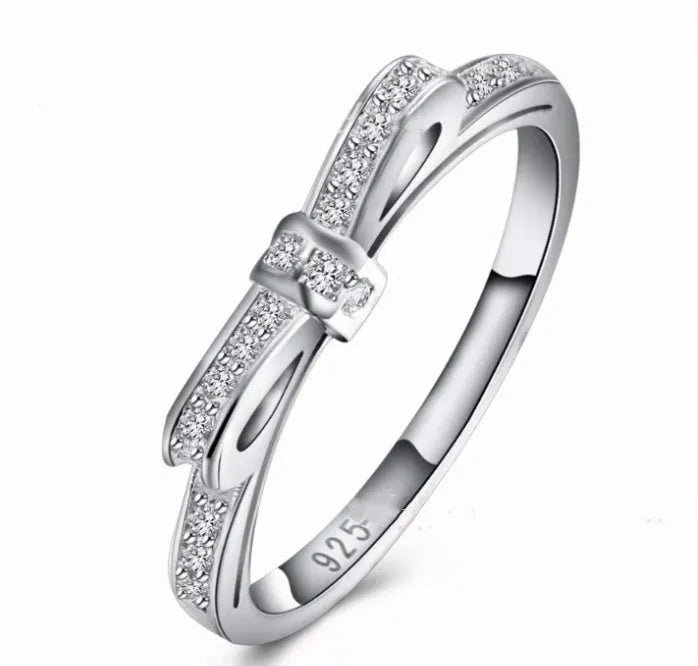 Silver electroplated bow ring with sparkling zircon crystals on a finger.