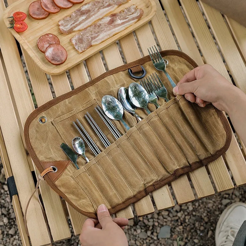 Green waxed canvas tableware storage bag containing wooden handle knives, forks, spoons, and chopsticks for outdoor use.