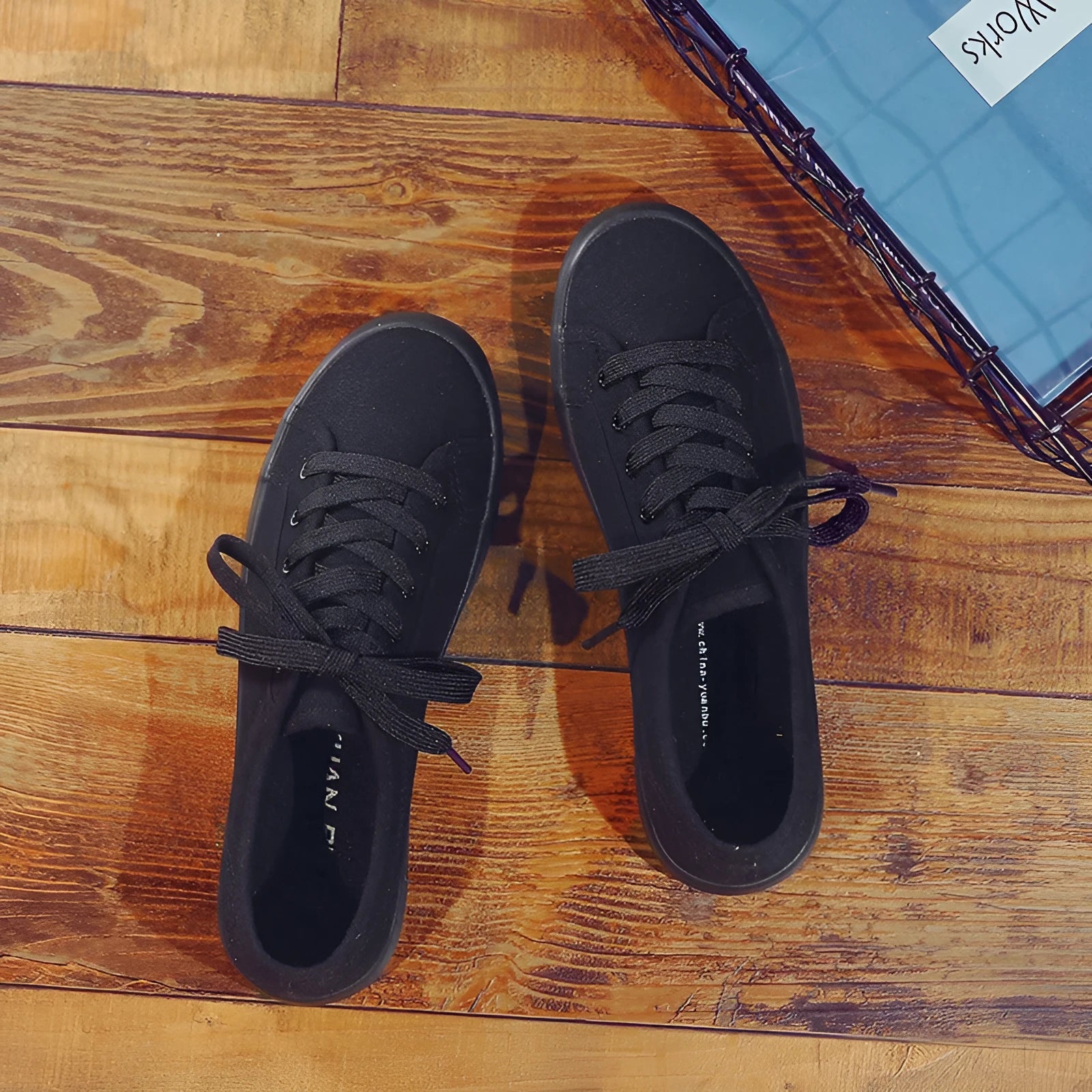 All black women's flat canvas shoes with white laces on a flat rubber sole.
