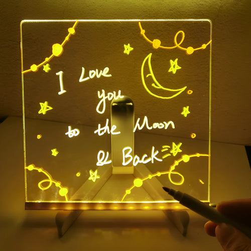 DIY acrylic LED message board lamp on a desk with colourful writing, showing USB cable and pens.