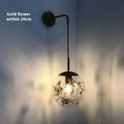 Modern glass wall mounted bedside lamp in golden flower finish on a white wall.