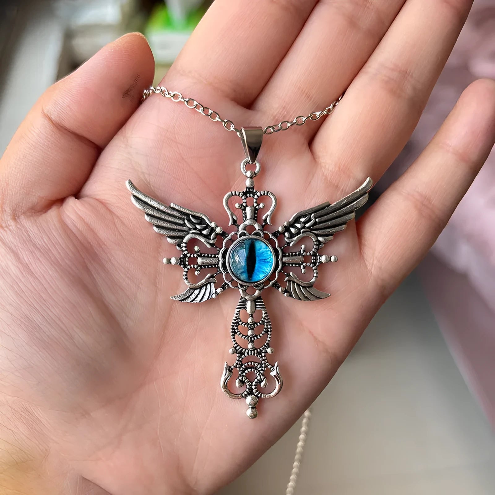 Close-up of a devil wings and cross design alloy pendant necklace on a chain, shown in a choice of colours.