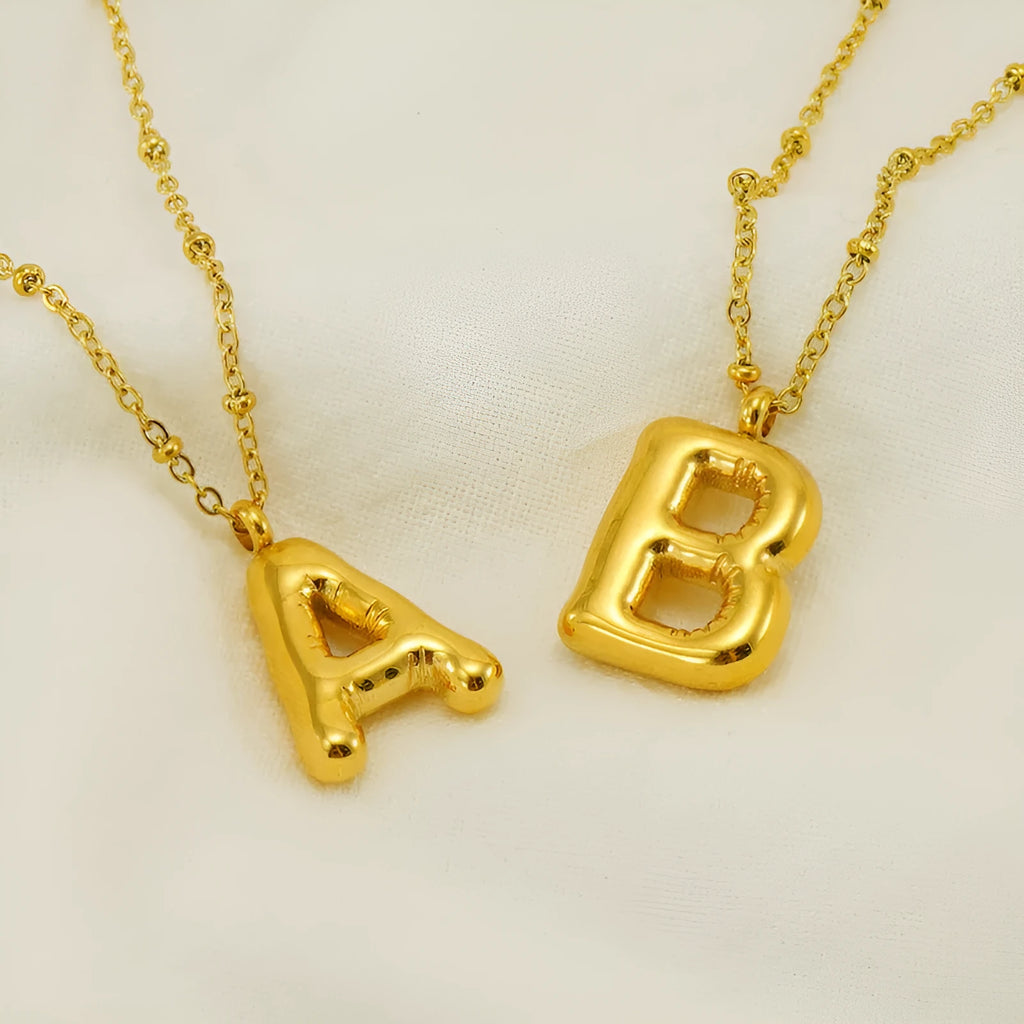 Gold bubble letter N pendant on stainless steel clip beads chain necklace against white background