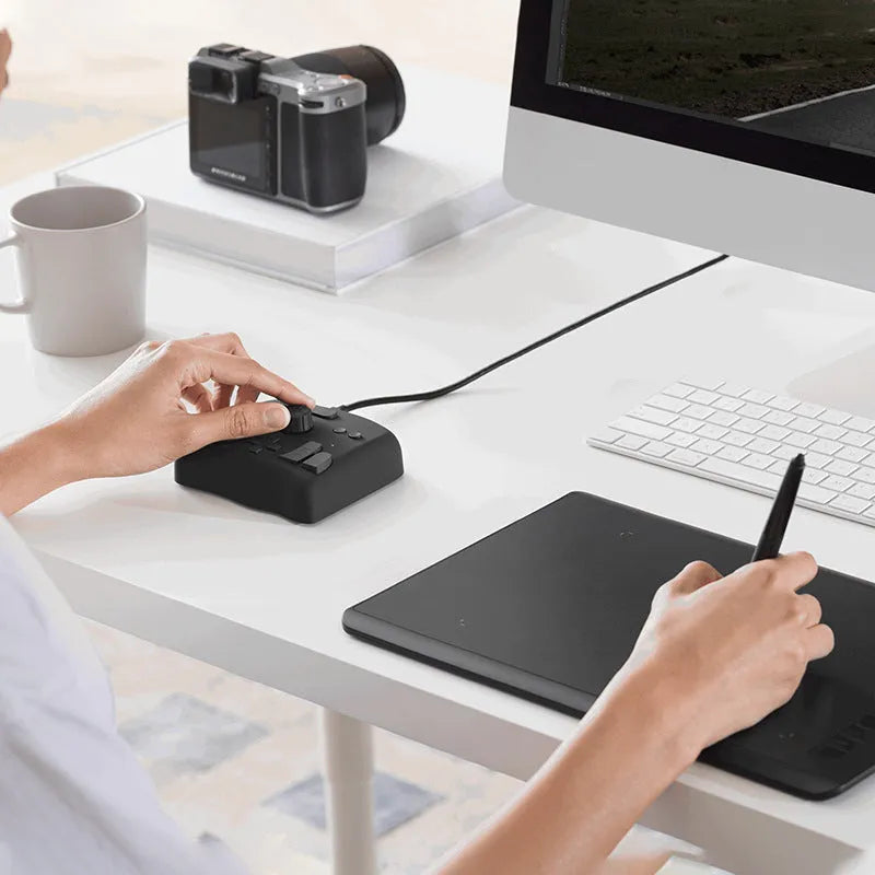 TourBox NEO auxiliary keyboard and video editing controller on a desk next to a laptop.