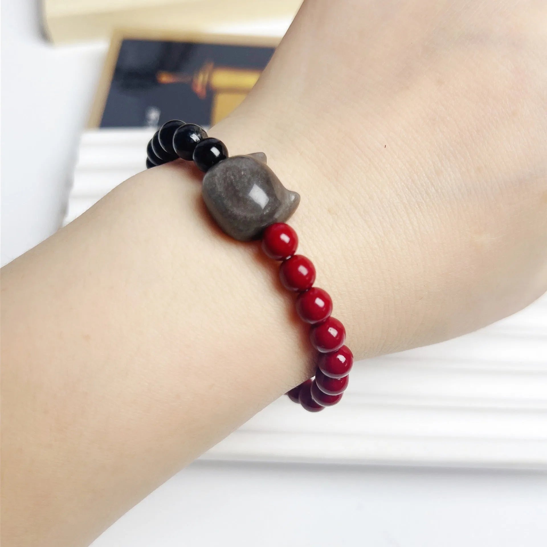 Black obsidian cat bracelet with golden crown charm and red bead on elastic cord