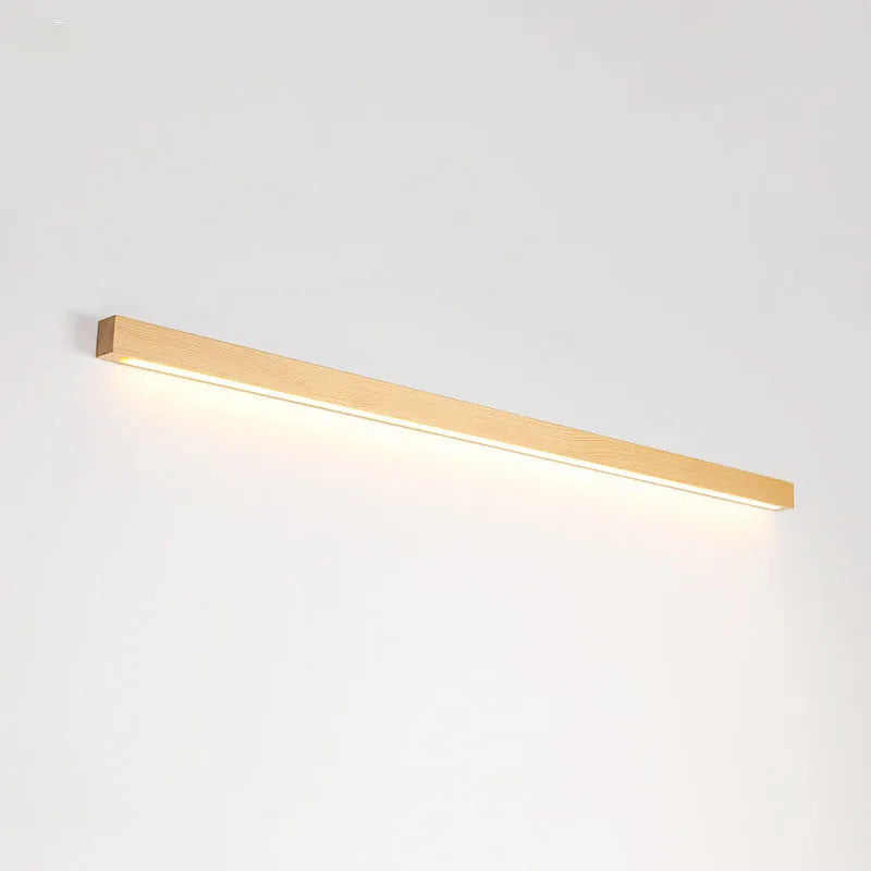 Long, slim walnut-coloured wooden wall lamp with integrated LED light, shown in a minimalist room setting.