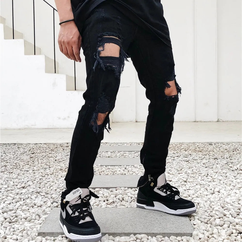 Men's high street style black torn jeans in washed black denim with raw edge details, front view.