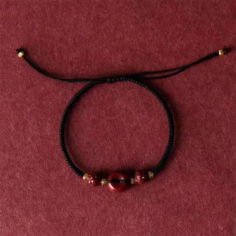 Traditional cinnabar bracelet with a heart-shaped peace buckle clasp on a red rope.