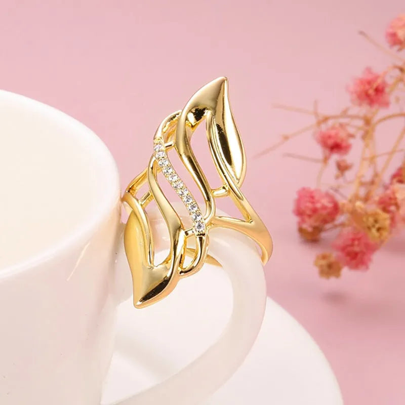 Gold tone women's ring with an exaggerated curved design on a model's finger.