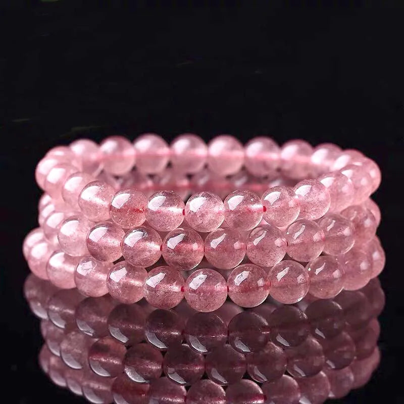 Women's strawberry quartz crystal bracelet with polished beads on a wrist.