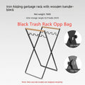 Black iron folding trash storage rack with a wooden handle for hanging bin bags.
