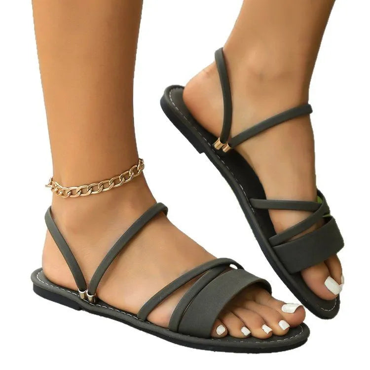 Women's flat sandal with cross strap and flip-toe buckle in black, showing round toe and rubber sole.