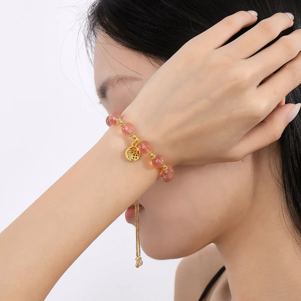 Close-up of a women's adjustable bracelet with pink strawberry quartz crystal beads and a silver fu charm on a geometric chain.
