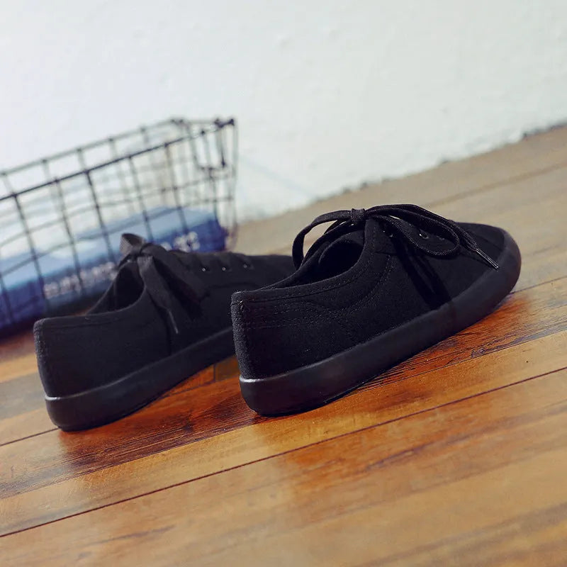 All black women's flat canvas shoes with white laces on a flat rubber sole.