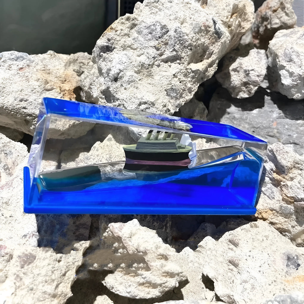 Fluid drift bottle with floating astronaut decoration in acrylic resin, black pearl pirate ship style, on a wooden desk.