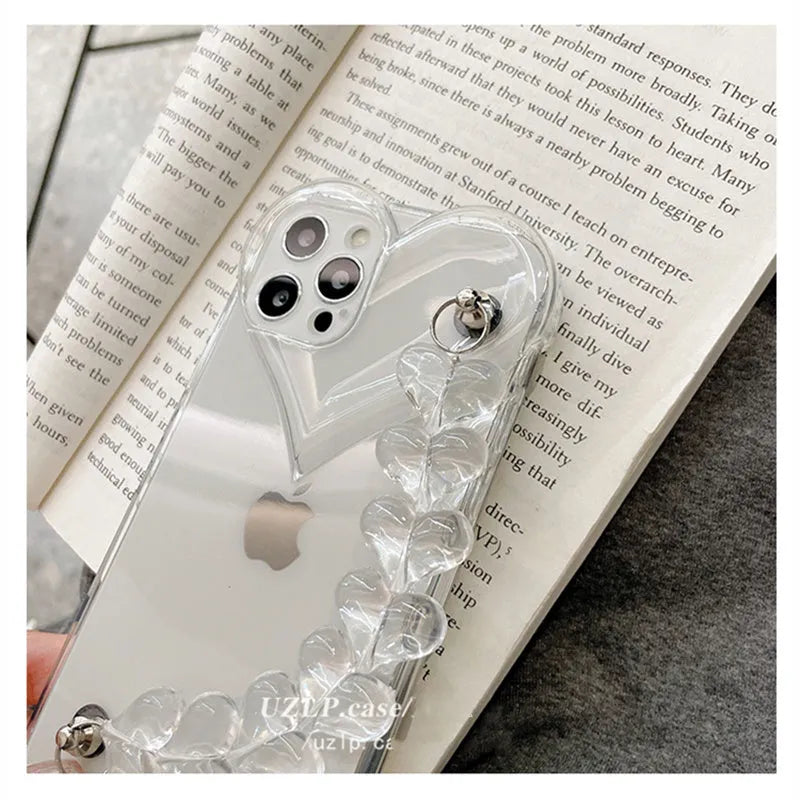 Clear iPhone case with transparent love heart bracelet charm attached, showing soft TPU material.