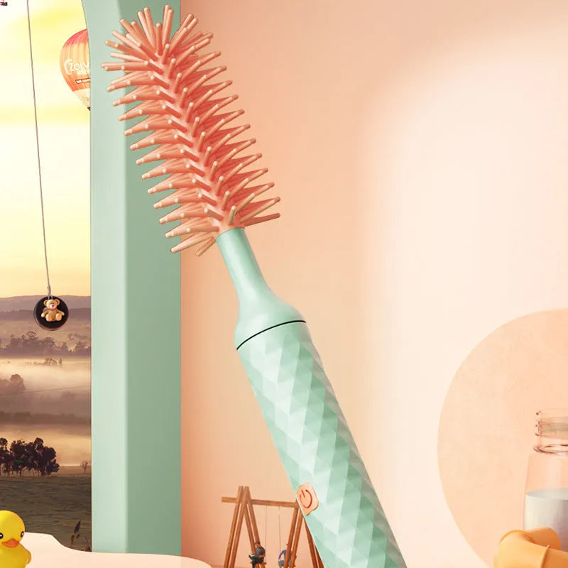 Pink and green electric baby bottle cleaning brush with rotating silicone head on a table