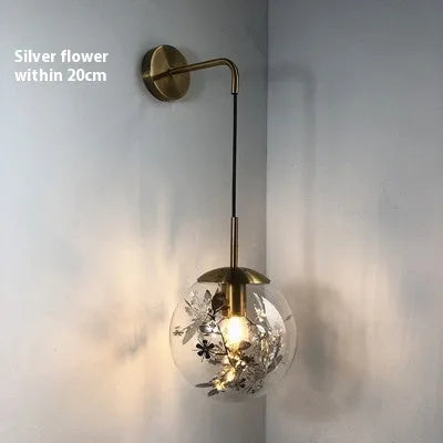 Modern glass wall mounted bedside lamp in golden flower finish on a white wall.