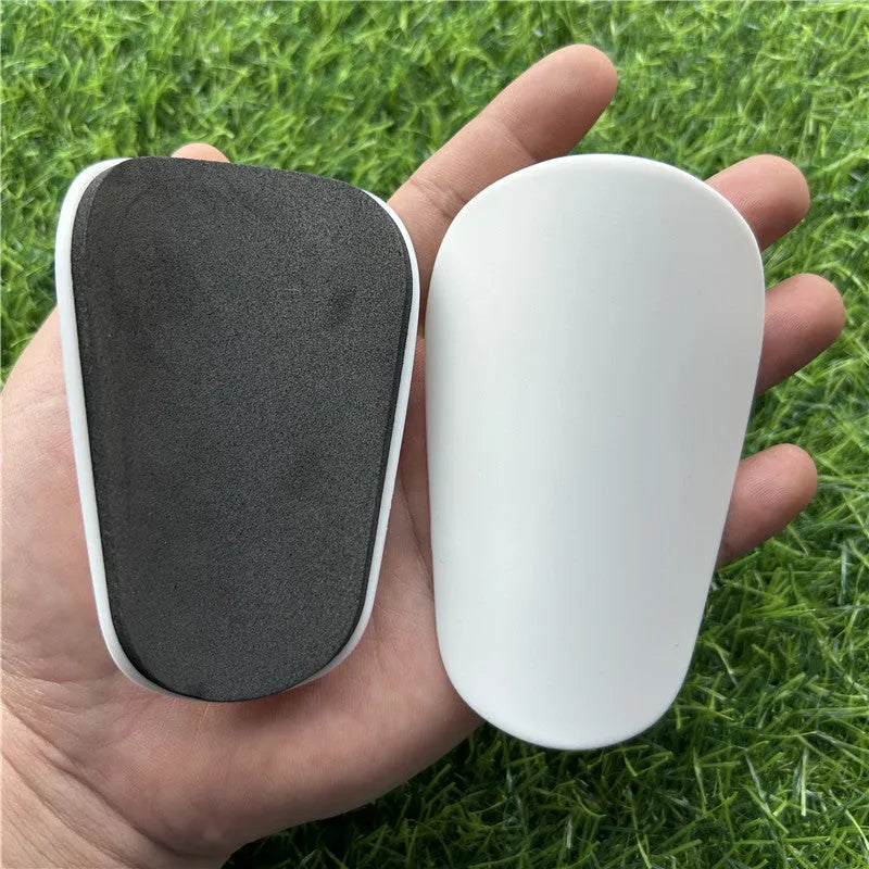 Pair of extra small black and white plastic football shin guards, measuring 8cm by 5cm.