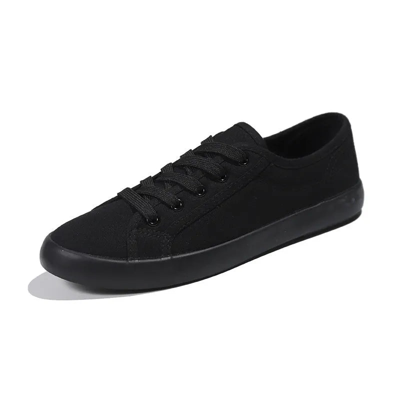All black women's flat canvas shoes with white laces on a flat rubber sole.