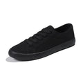 All black women's flat canvas shoes with white laces on a flat rubber sole.