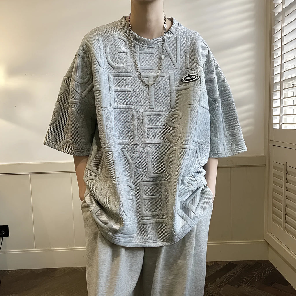 Men's grey loose-fit short sleeve t-shirt featuring a raised three-dimensional letter design on the front.