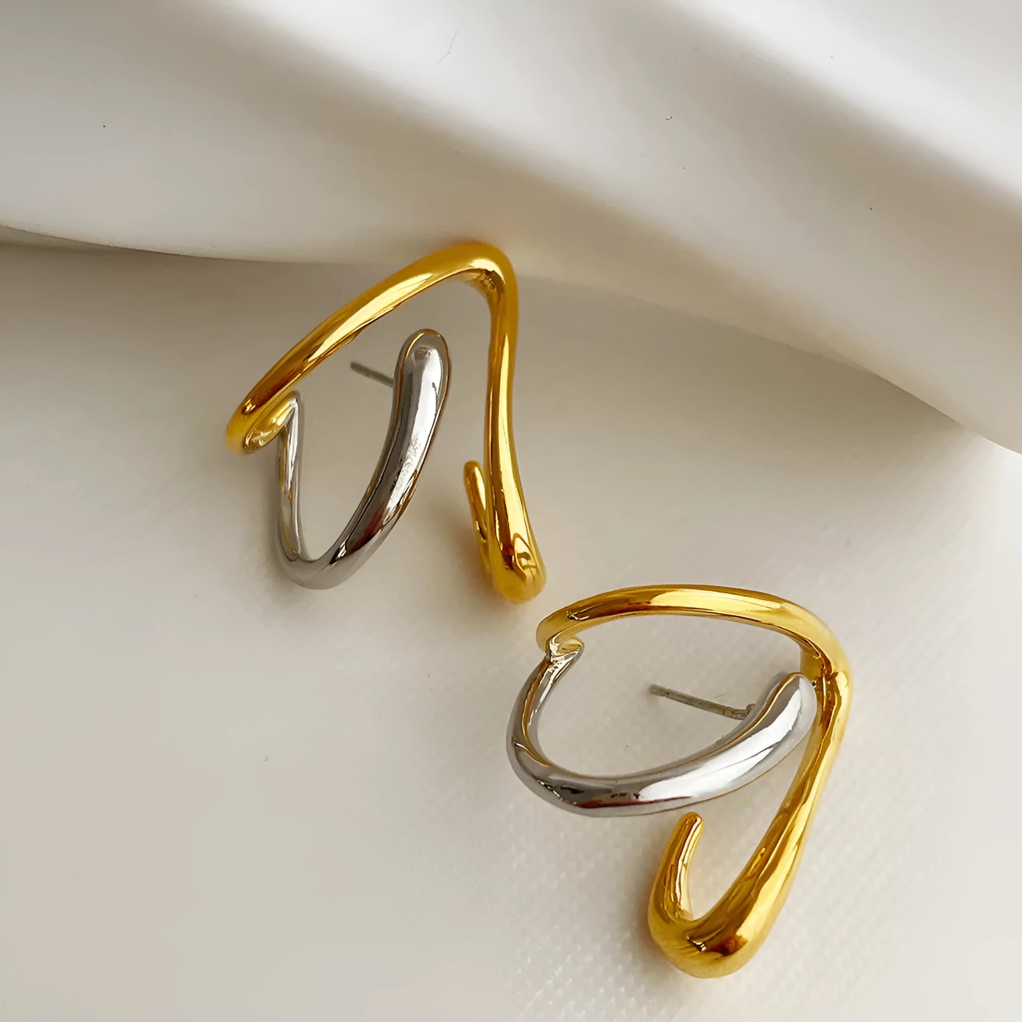 Gold and silver irregular triangle alloy stud earrings with sterling silver needle on neutral background