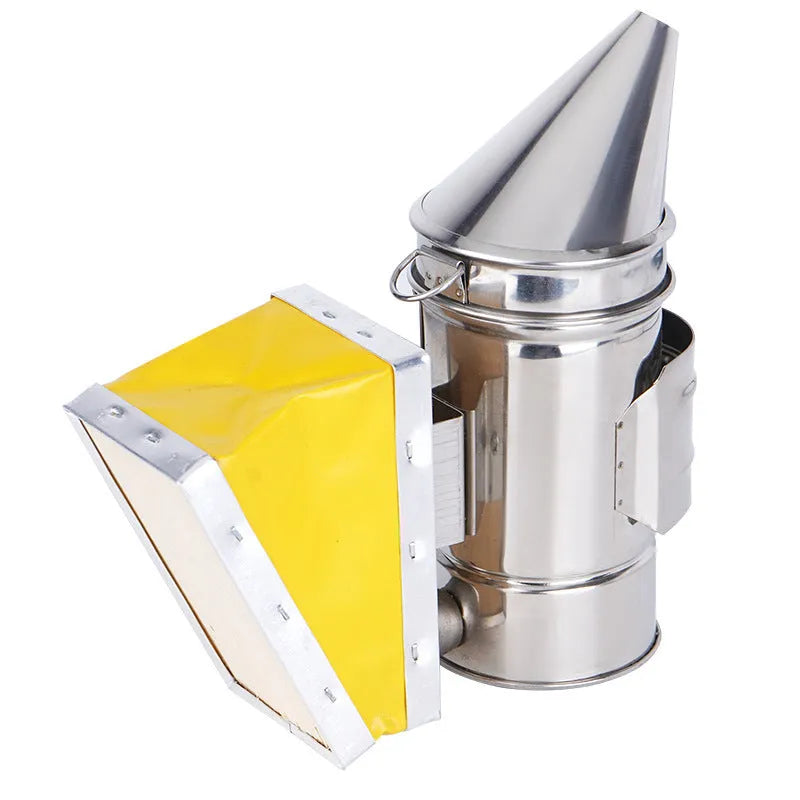 Stainless steel bee smoker with leather bellow on a wooden table against a blurred outdoor background