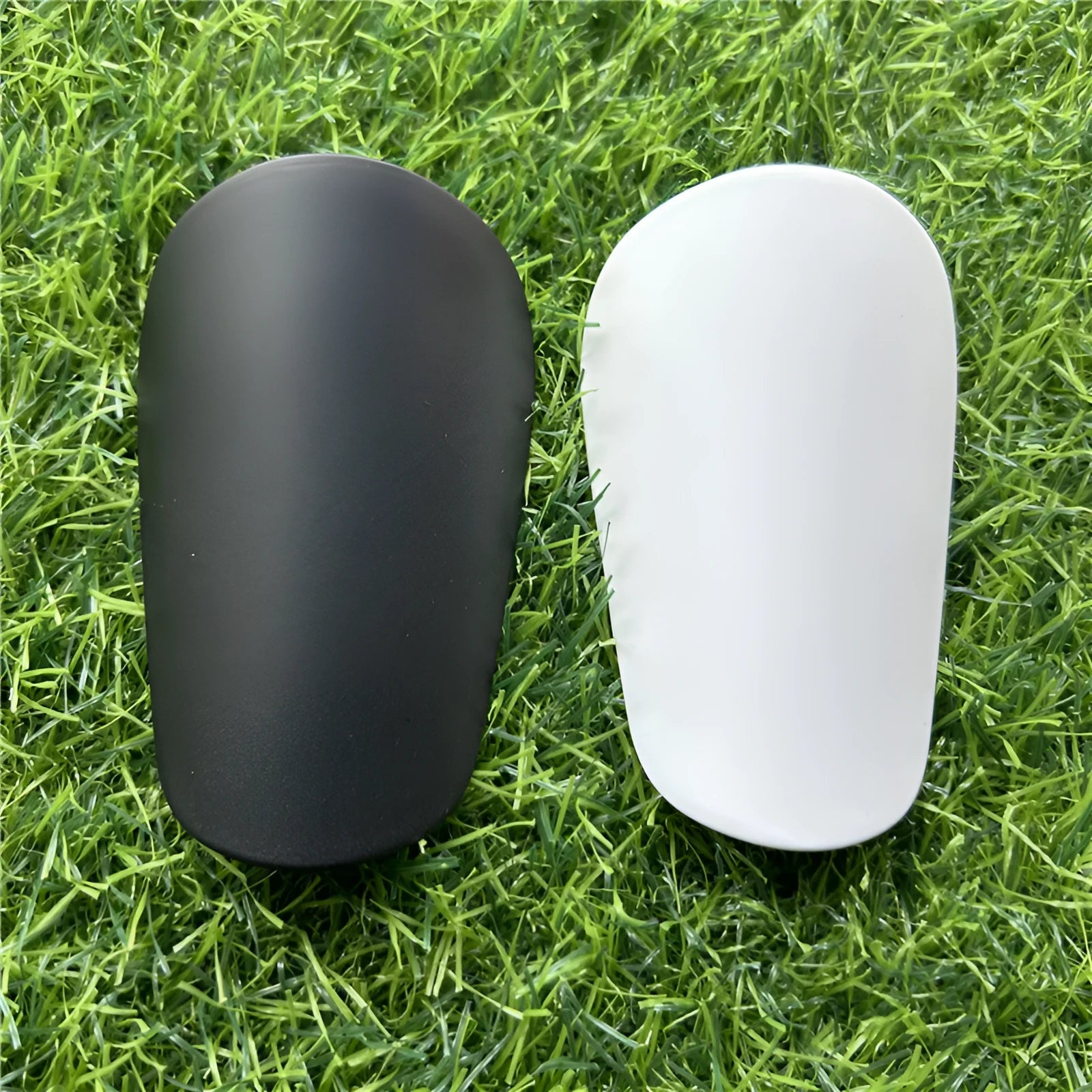 Pair of extra small black and white plastic football shin guards, measuring 8cm by 5cm.