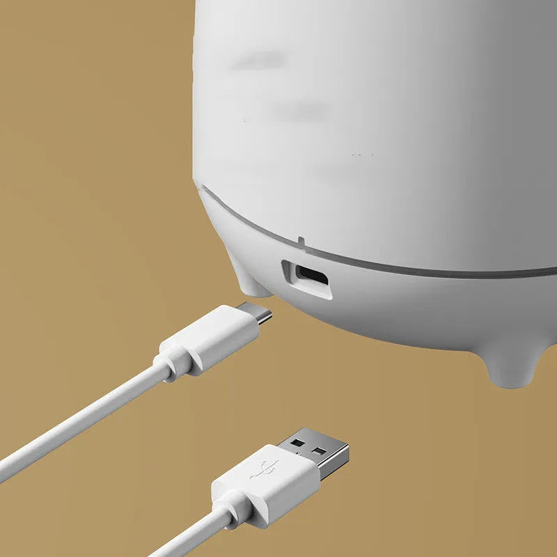 White volcano-shaped ultrasonic humidifier with USB cable on a wooden desk.