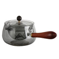 Transparent rotary glass teapot with wooden handle and built-in tea infuser on a table.