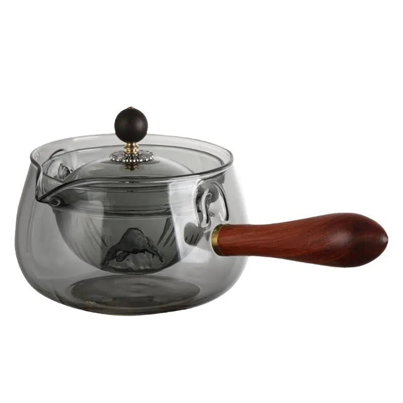 Transparent rotary glass teapot with wooden handle and built-in tea infuser on a table.