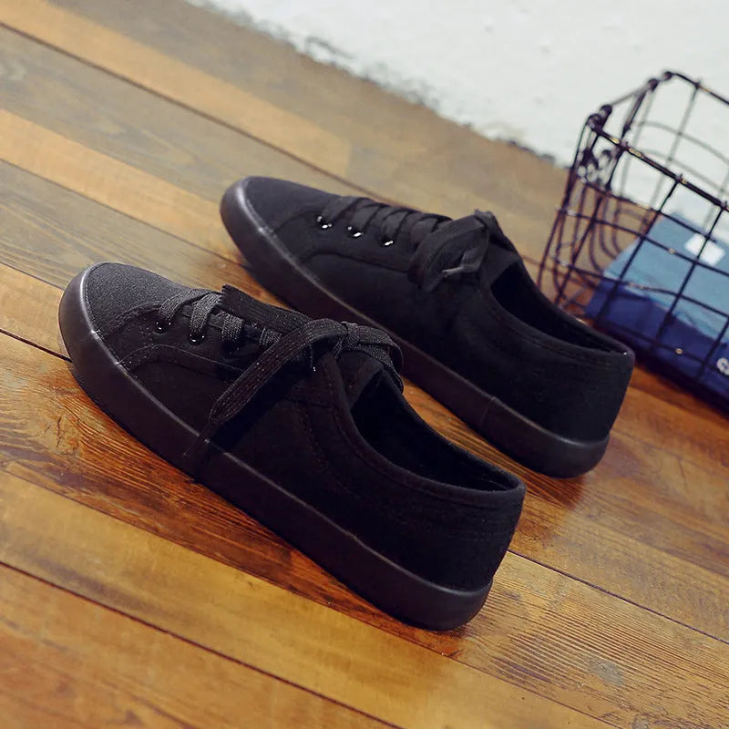 All black women's flat canvas shoes with white laces on a flat rubber sole.
