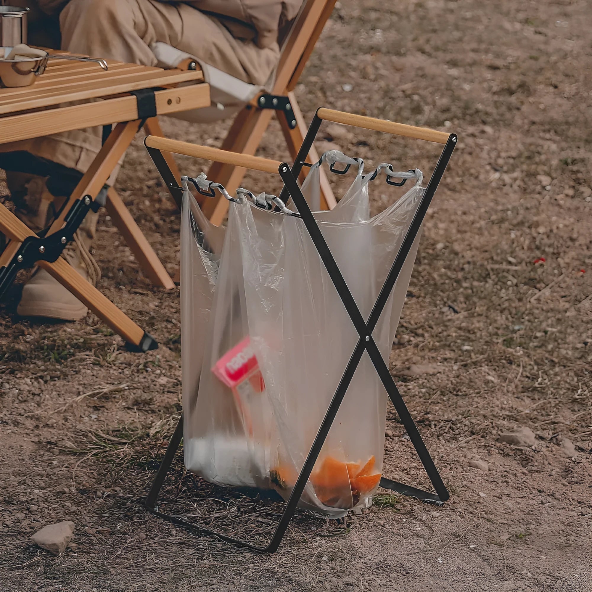 Black iron folding trash storage rack with a wooden handle for hanging bin bags.