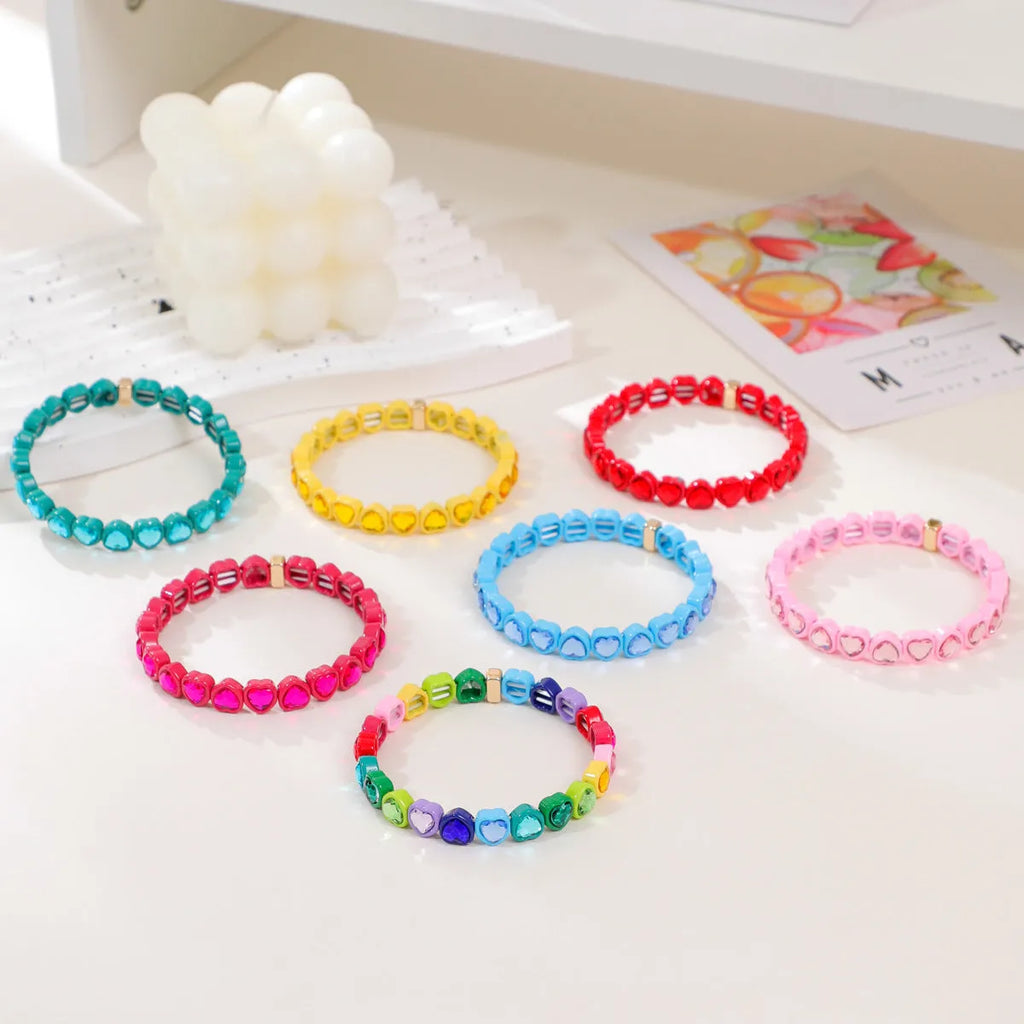 Colourful rainbow enamel heart-shaped stretch bracelet on a wrist.