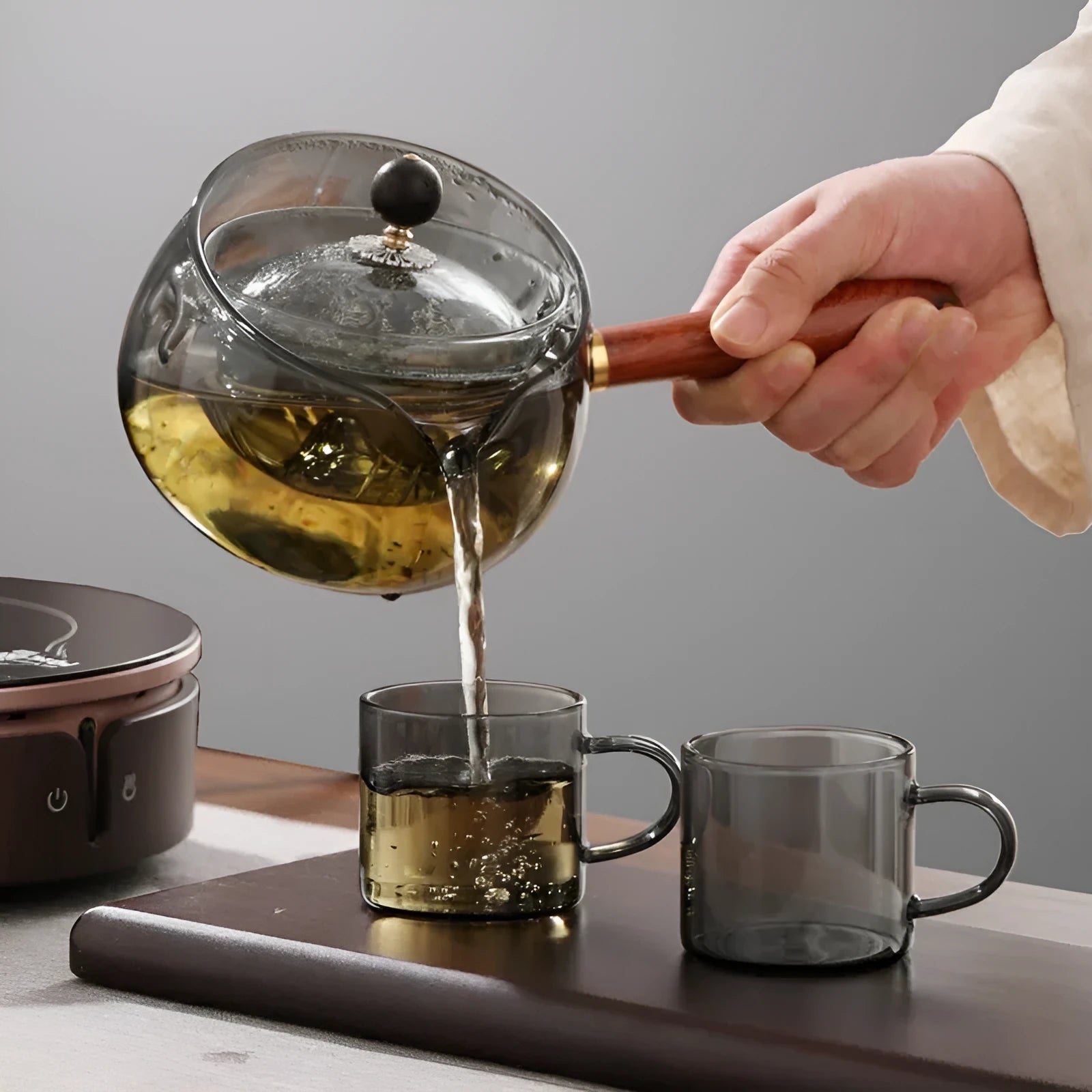 Transparent rotary glass teapot with wooden handle and built-in tea infuser on a table.