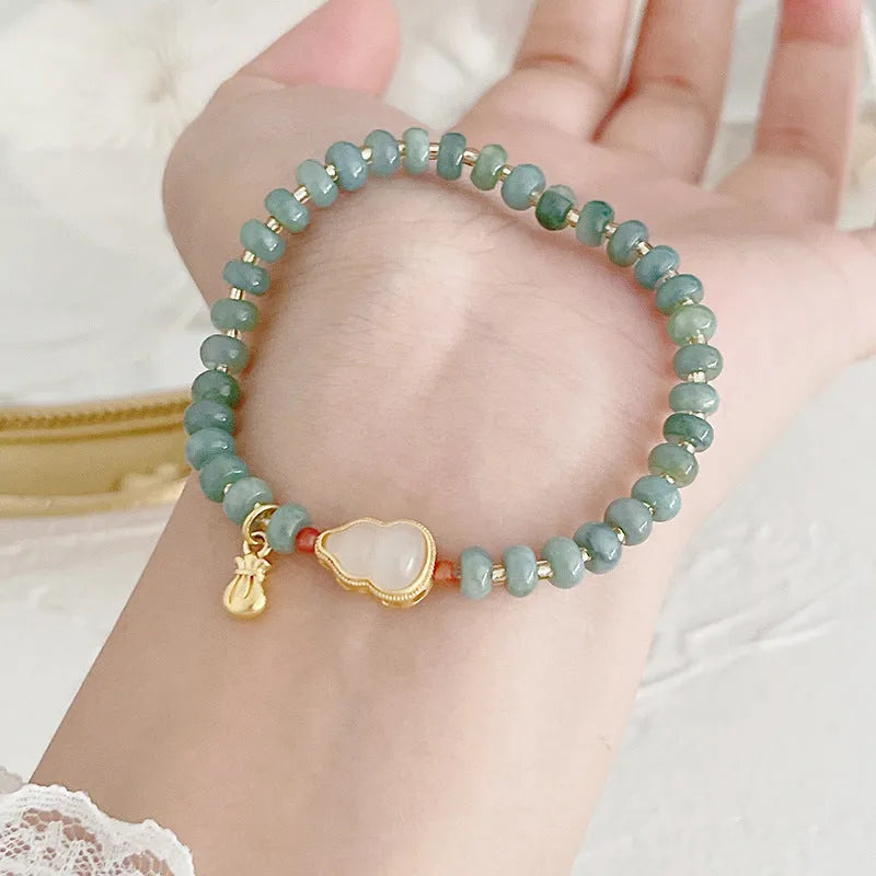 Close-up of a blue jade women's bracelet showing a gourd charm and a peace buckle charm on a string.